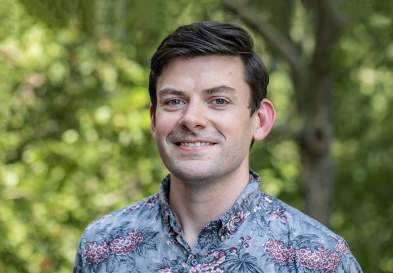 Standing in front of greenery John Nelson business student is smiling