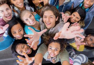 Excited diverse male and female college students celebrate the end of the semester. They are reaching up toward the camera.