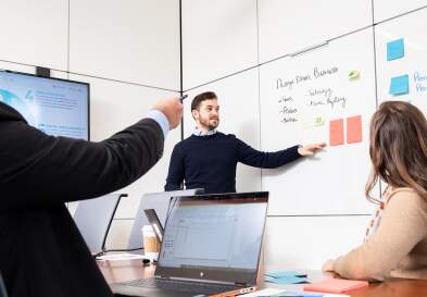 Three students around table discuss marketing terms written on whiteboard