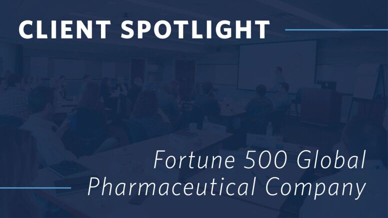 A graphic showing the words “Client Spotlight: Fortune 500 Global Pharmaceutical Company” overlaid on an image of businesspeople sitting around a conference table during a presentation.