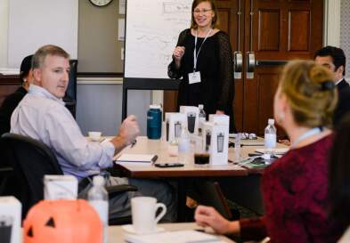 UNC professor Heidi Schultz giving a presentation to businesspeople seated at a conference table.