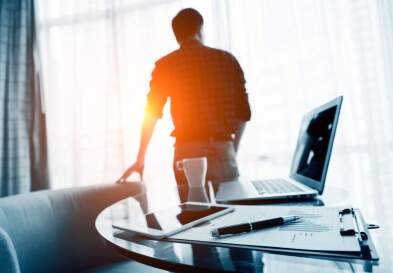 A businessman stepping away from a desk while looking toward a window.
