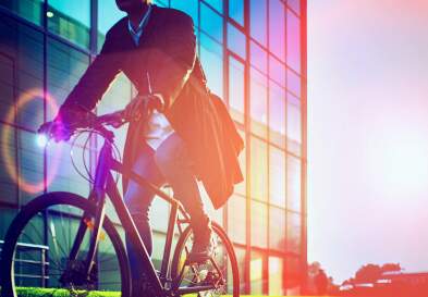 Man, on the way to work, riding bicycle beside the modern office building.