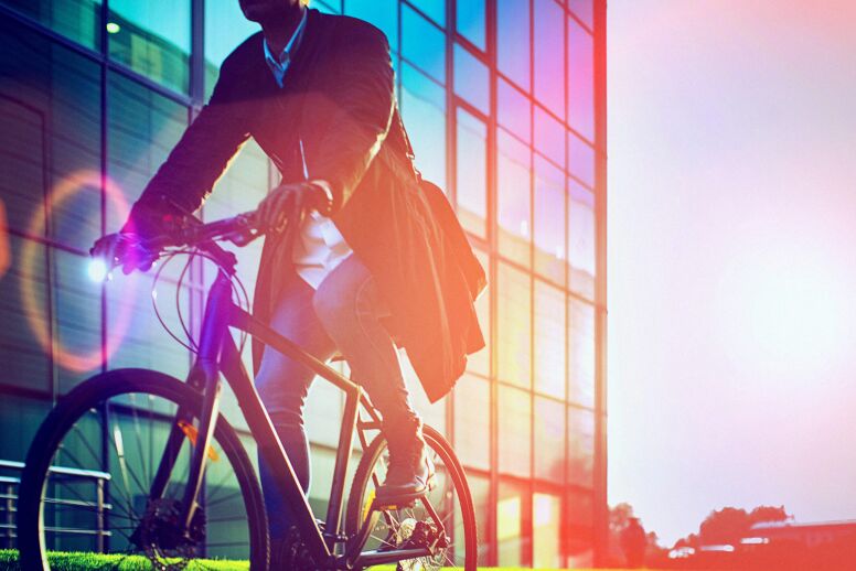 Man, on the way to work, riding bicycle beside the modern office building.