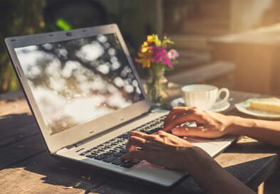Closeup of hands typing on a laptop while the person works outside with coffee.