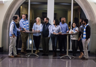 MAC students stand around tall tables while talking to each other