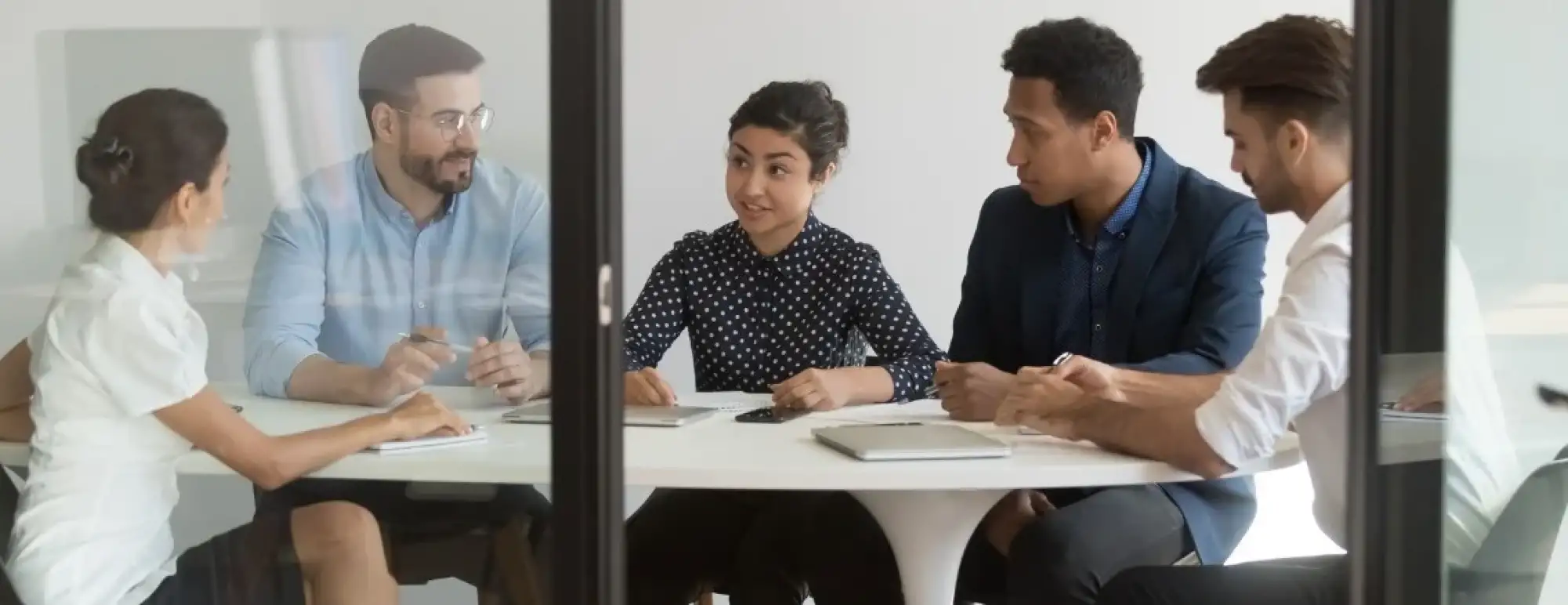 Five businesspeople sit around a table discussing a project.