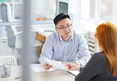 Businessman and businesswoman sitting at a desk in an office having a discussion.