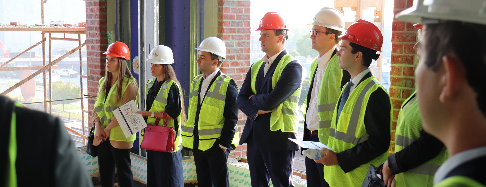 A group of 8 real estate students wearing hard hats listen to a speaker on an active construction site.
