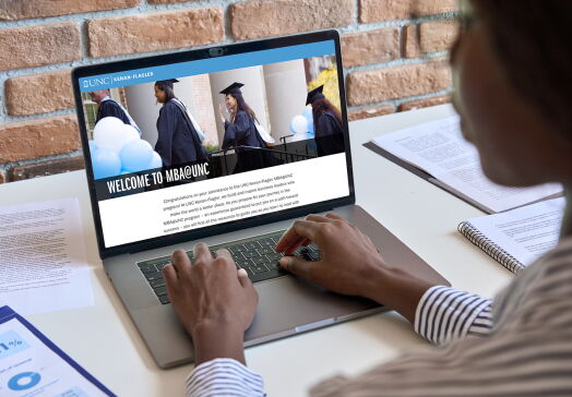 Student typing on laptop with MBA@UNC program featured on screen