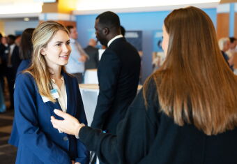 Two women in professional dress chatting in a busy networking session.