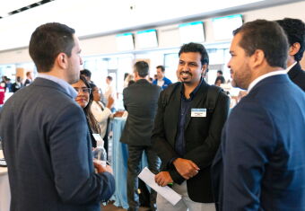 A group of four young professionals standing in a group smiling and chatting with a recruiter.