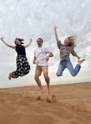 Three students on a sand dune jumping in the air