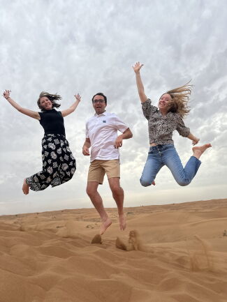 Three students on a sand dune jumping in the air