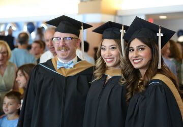 Three MAC graduates smile in their robes and caps.