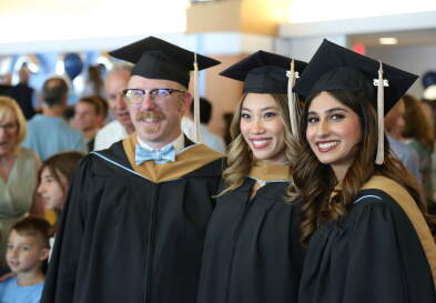 Three MAC graduates smile in their robes and caps.