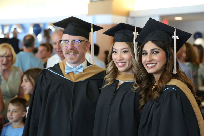 Three MAC graduates smile in their robes and caps.