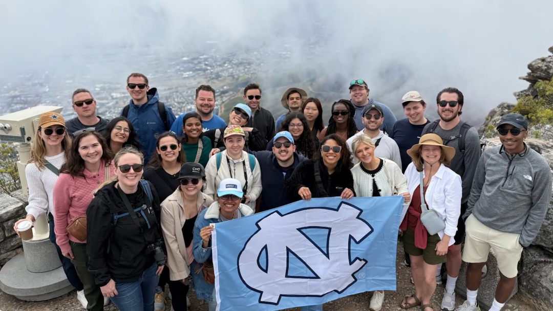 A group of MBA students at the top of a mountain smiling at the camera holding a UNC flag