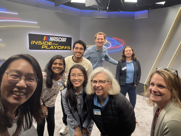 Seven students and a faculty member taking a group selfie on a company visit
