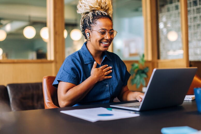 A woman in a blue shirt is sitting in front of a laptop smiling. She appears to be talking to the computer.