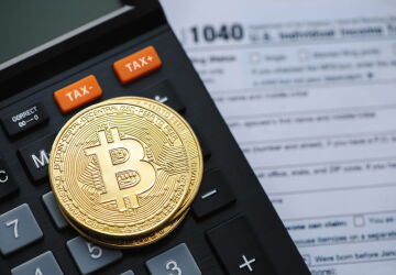 Bitcoin on top of a calculator and tax return.