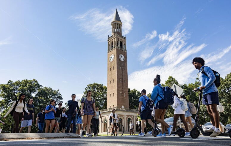The Bell Tower against a Carolina blue sky with students crossing the street in front of it.