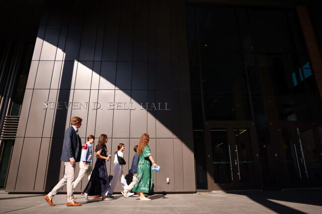 Attendees of the grand opening walk in the sunlight underneath the Steven D. Bell Hall lettering outside of the entrance.