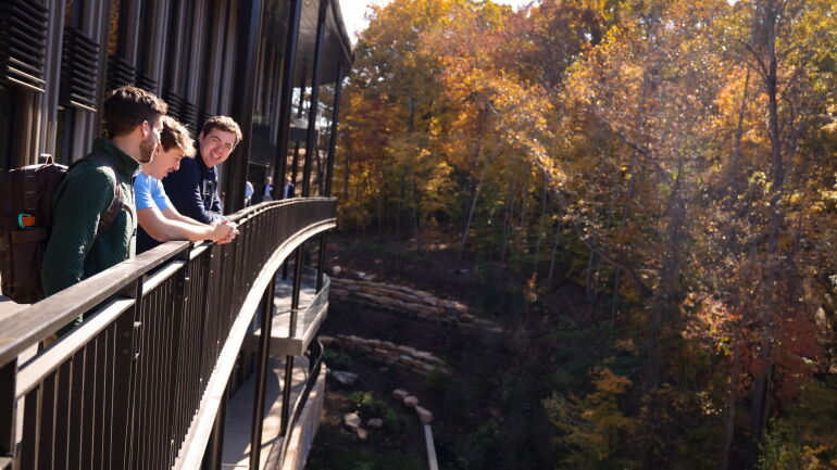 Three students overlook the landscaping surrounding Bell Hall from the walkway.