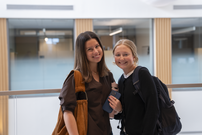 Two students pose for a photo against a glass railing in Bell Hall.