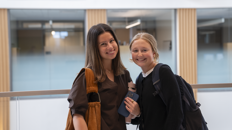 Two students pose for a photo against a glass railing in Bell Hall.