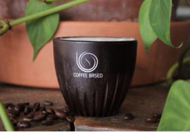 Cup of coffee surrounded by plants with beans on table