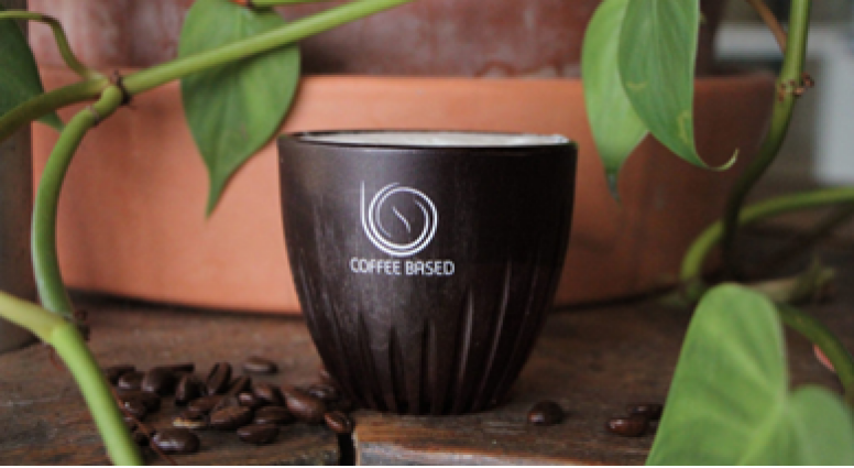 Cup of coffee surrounded by plants with beans on table