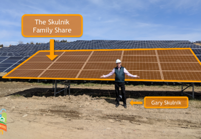 Gary Skulnik standing in front of solar farm, arms outstretched