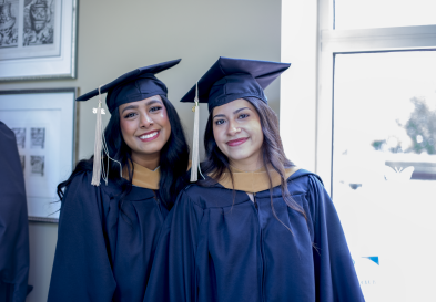 Two MAC graduates smile in their regalia.