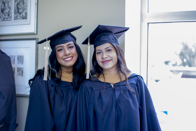 Two MAC graduates smile in their regalia.