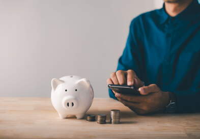 Person uses a smartphone next to a piggy bank.